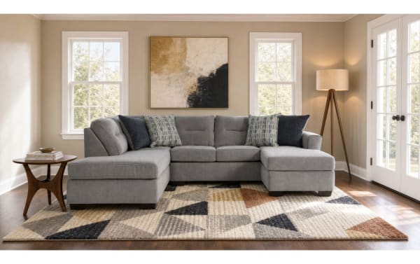 Modern living room with a gray fabric sectional sofa featuring chaise lounges on both ends, geometric patterned area rug, wooden side table, and tripod floor lamp.